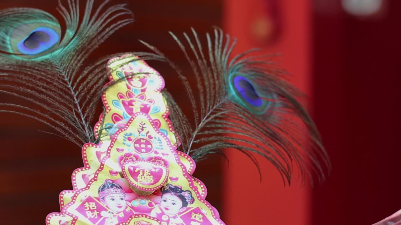 A vibrant pyramid structure adorned with peacock feathers against a rich red background.