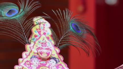 a vibrant pyramid structure adorned with peacock feathers against a rich red background.