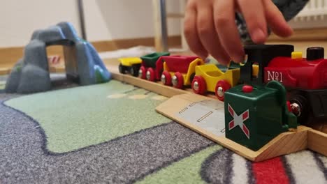 a faceless child playing with colorful wooden train, moving it back and forth in the wooden train rail