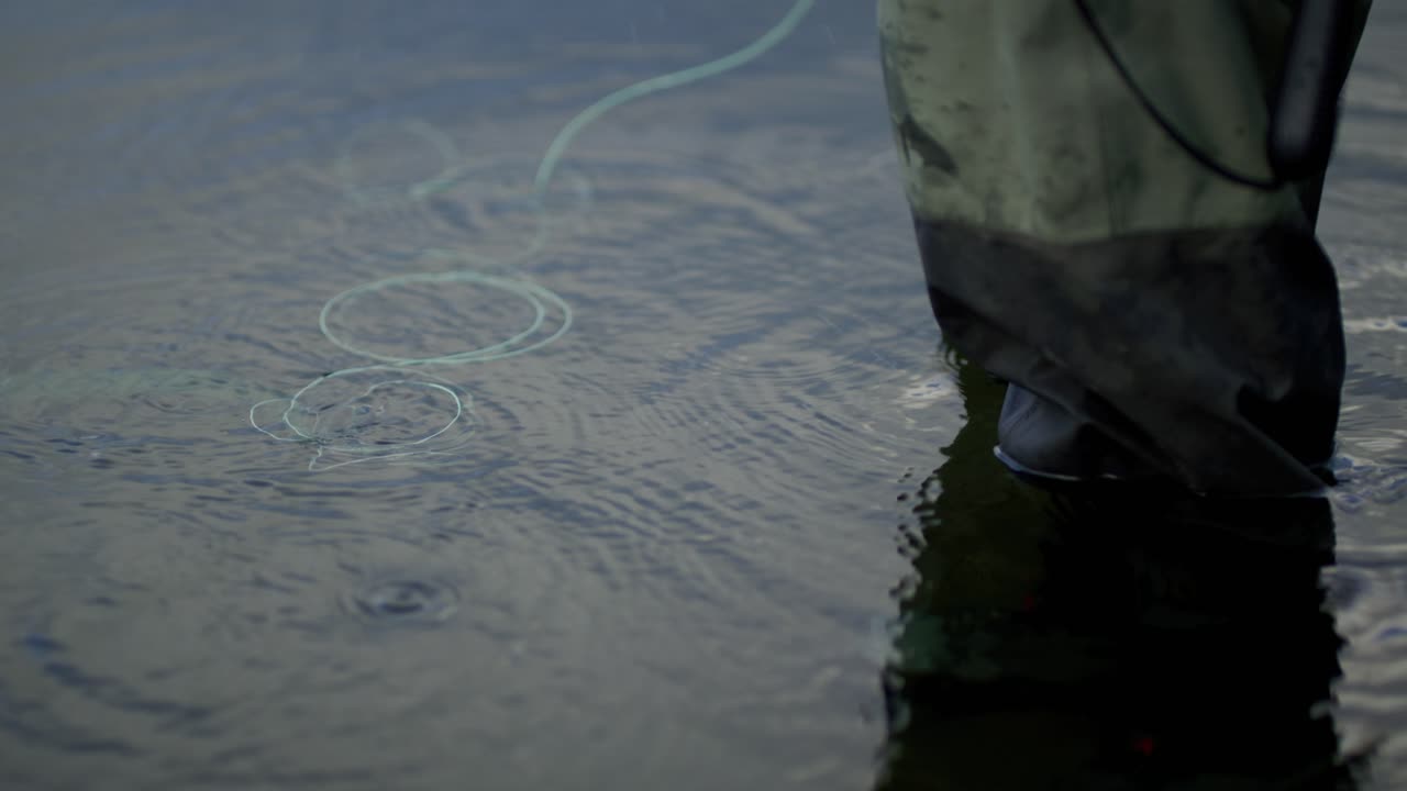 Line floats by legs of man fly fishing in shallow water, close view
