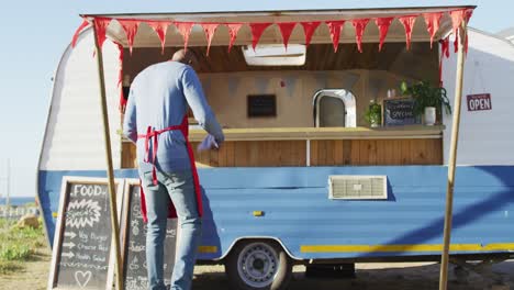 Rear-view-of-african-american-man-wearing-apron-smiling-while-cleaning-the-food-truck