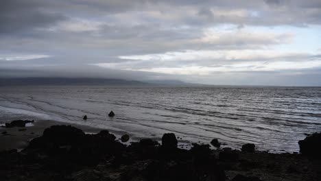 Timelapse-of-waves-crashing-on-a-sandy-beach,-rocks-on-the-seashore-,-cloudy-weather-in-Dundalk,-Ireland