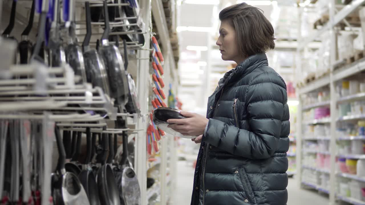 mujer joven comprando en el supermercado eligiendo sartén