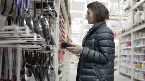 young woman shopping in grocery chosing frying pan