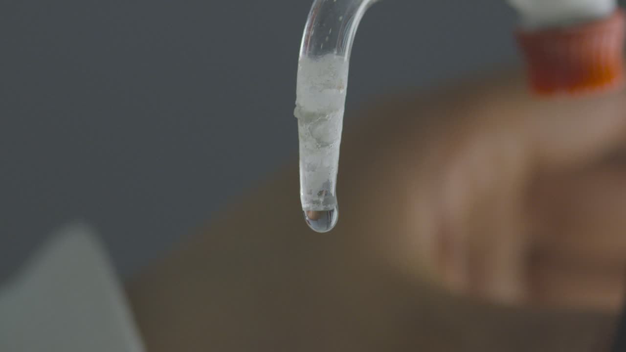 Detailed close-up of a drop of liquid descending from a burette in a laboratory setting.