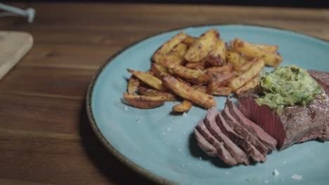 carne cortada con papas fritas, acompañada de mantequilla de café de parís, servida en un plato azul