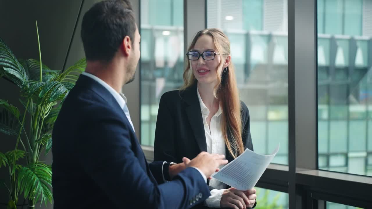 Two professional colleagues a man and a woman in formal suits in bright office space discussing a business strategy and exchanging ideas
