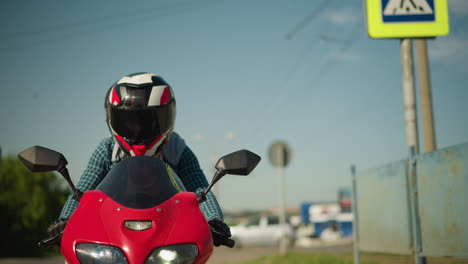 two sisters ride together on a red power bike, both wearing helmets. in the background, cars are seen making turns and moving along an urban road, with a large building in view