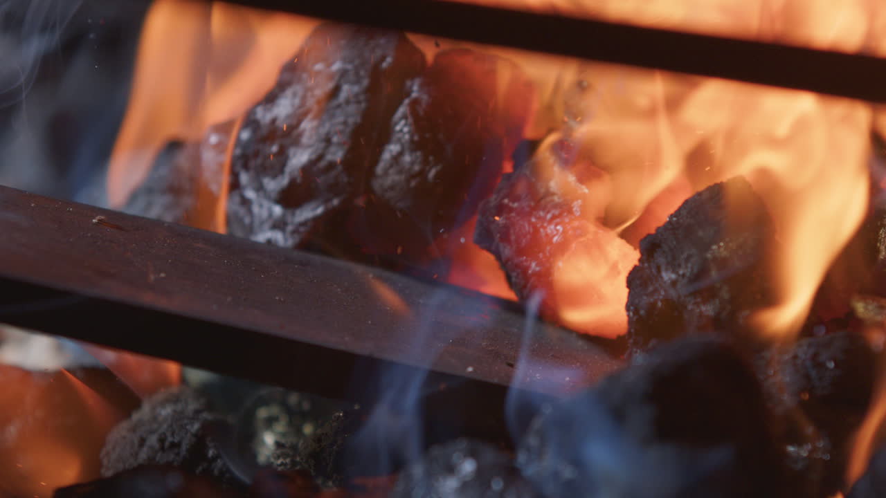 Hot burning coals adjusted around metal piece in blacksmith's forge, close-up