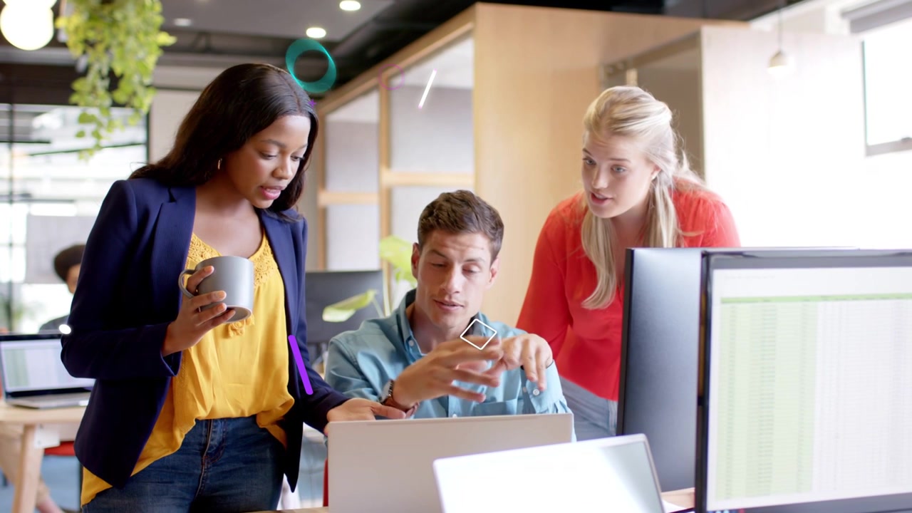 Three coworkers at laptop, left woman leaning with mug initiating man explaining spreadsheet