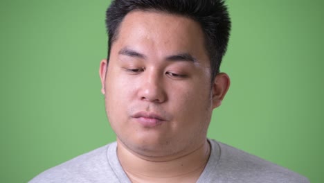 young handsome overweight asian man against green background