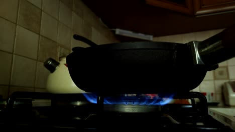 close-up of a kitchen gas stove with a burner on and a frying pan on it. the gas burner under the pan burns with a blue flame.