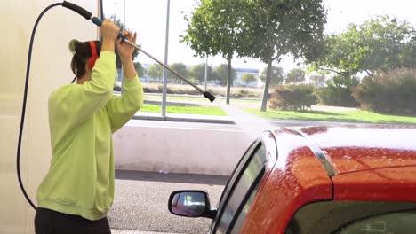 mujer limpiando el capó del coche rojo con manguera de presión y escuchando música con auriculares rojos