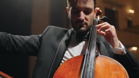 concentrated violoncellist is playing cello on scene of music hall concert or rehearsal of symphonic orchestra