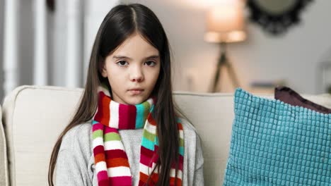 close up portrait of sick little girl wearing a warm scarf  and looking at camera while sitting at home alone