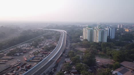 Toma-Cinematográfica-Reveladora-De-Majerhat-Recién-Construido-Sobre-La-Carretera-Del-Puente-Con-Garaje-De-Hierro-En-El-Lado-Izquierdo-Y-Edificios-De-Gran-Altura-En-El-Otro-Lado,-Toma-Aérea