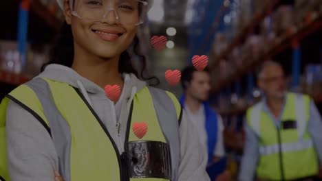 Animation-of-hearts-floating-over-happy-biracial-female-warehouse-worker