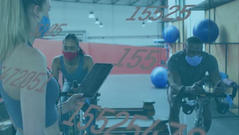 animation of numbers changing over female instructor, woman and man in face masks on bikes in gym