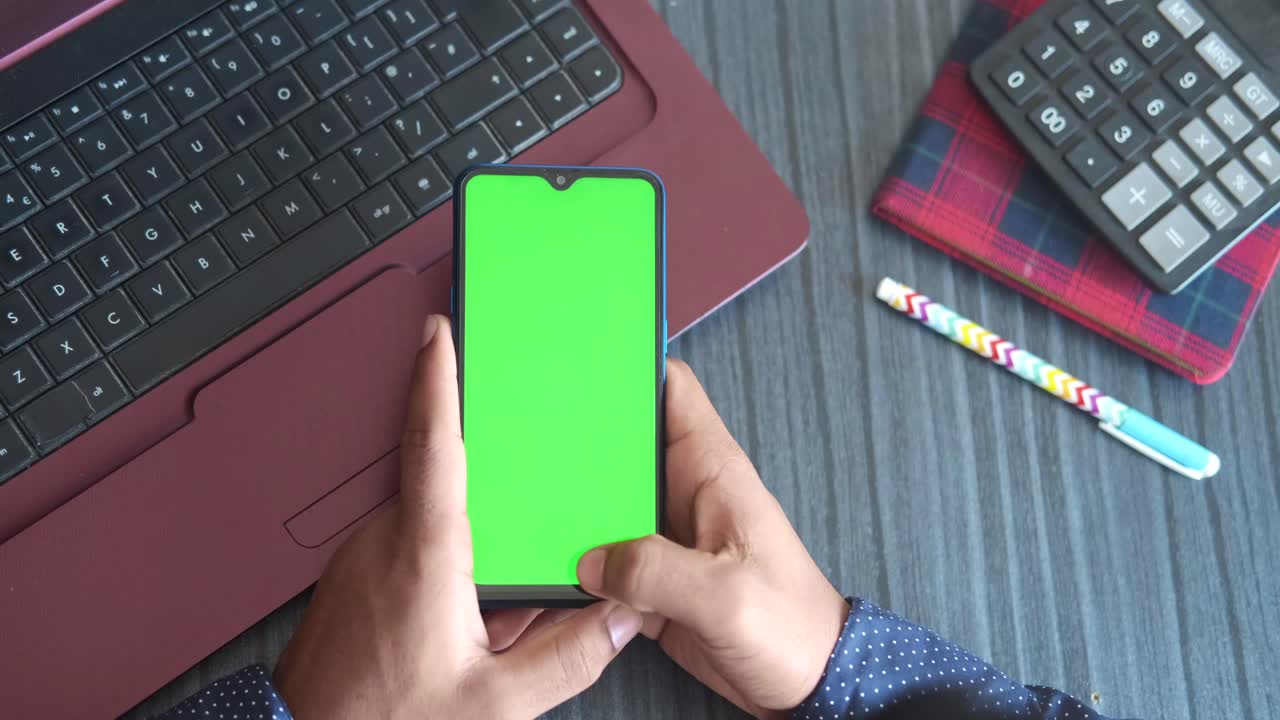 persona con un teléfono inteligente con pantalla verde, usando una computadora portátil y una calculadora