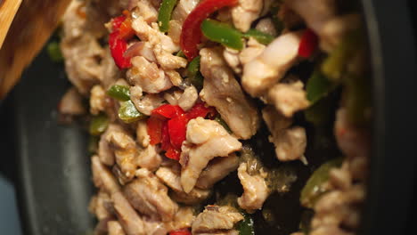 close up of wooden spoon mixing fajitas ingredients cooking in pan