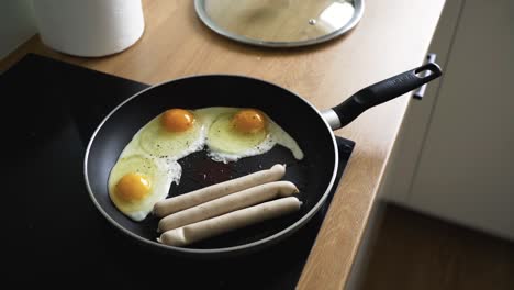 shot-of-black-hot-pan-on-electric-stove-with-omelet-and-frying-sausages-in-the-kitchen-at-home