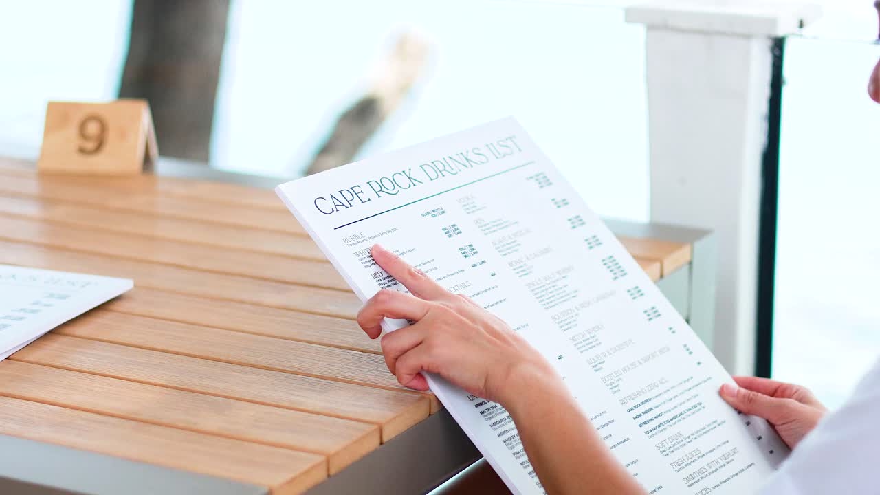 A woman examines a menu at a seaside restaurant in Phuket. Bright, natural lighting and a relaxed atmosphere enhance the scene