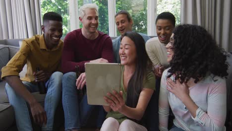 diverse group of happy male and female friends looking at tablet and laughing in living room