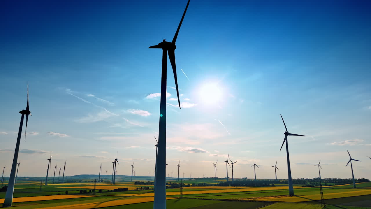 Silhouettes of tall wind turbines rotating in the wind. Low angle view at the windmills producing green energy.