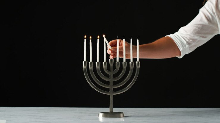 Hand lighting the remaining white candles in a Jewish menorah from a single candle, close up, front view