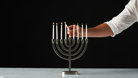 hand lighting the remaining white candles in a jewish menorah from a single candle, close up, front view