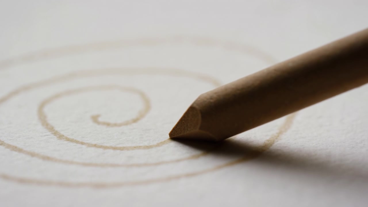 Eine Nahaufnahme zeigt einen gespitzten Holzbleistift, der eine durchgehende braun-graue Spirale auf leicht strukturiertem weißem Papier zeichnet, während geringe Tiefenschärfe die bewegliche Spitze vor weicher Umgebung scharf hält.