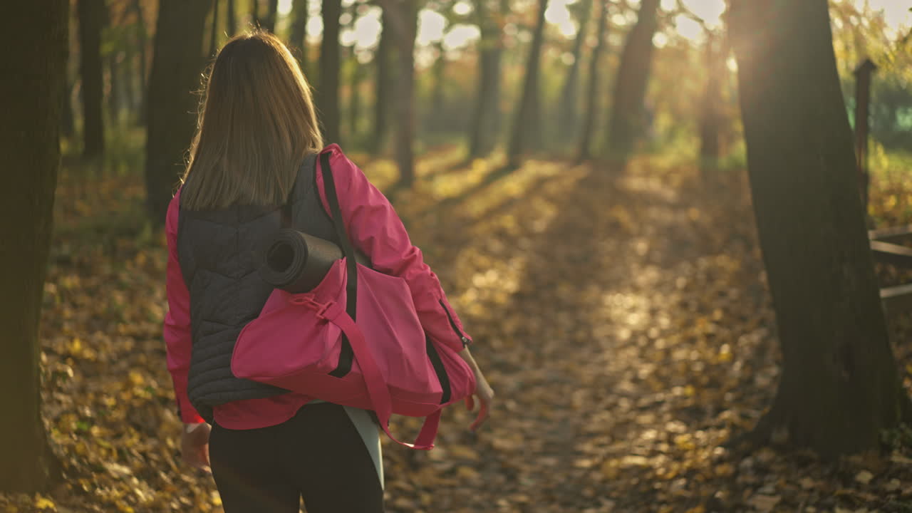 Woman Walking in Autumn Forest with Yoga Mat