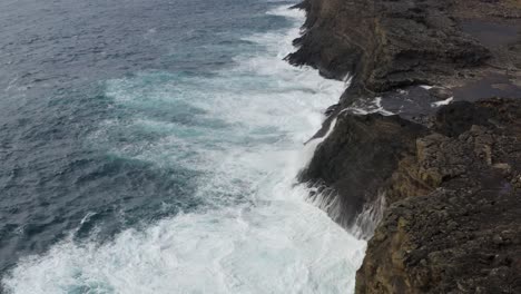 Toma-Aérea-De-Pájaros-De-Olas-Rompiendo-Contra-La-Costa-Rocosa-De-La-Isla-Vagar-Con-Cascada-Bösdalafossur