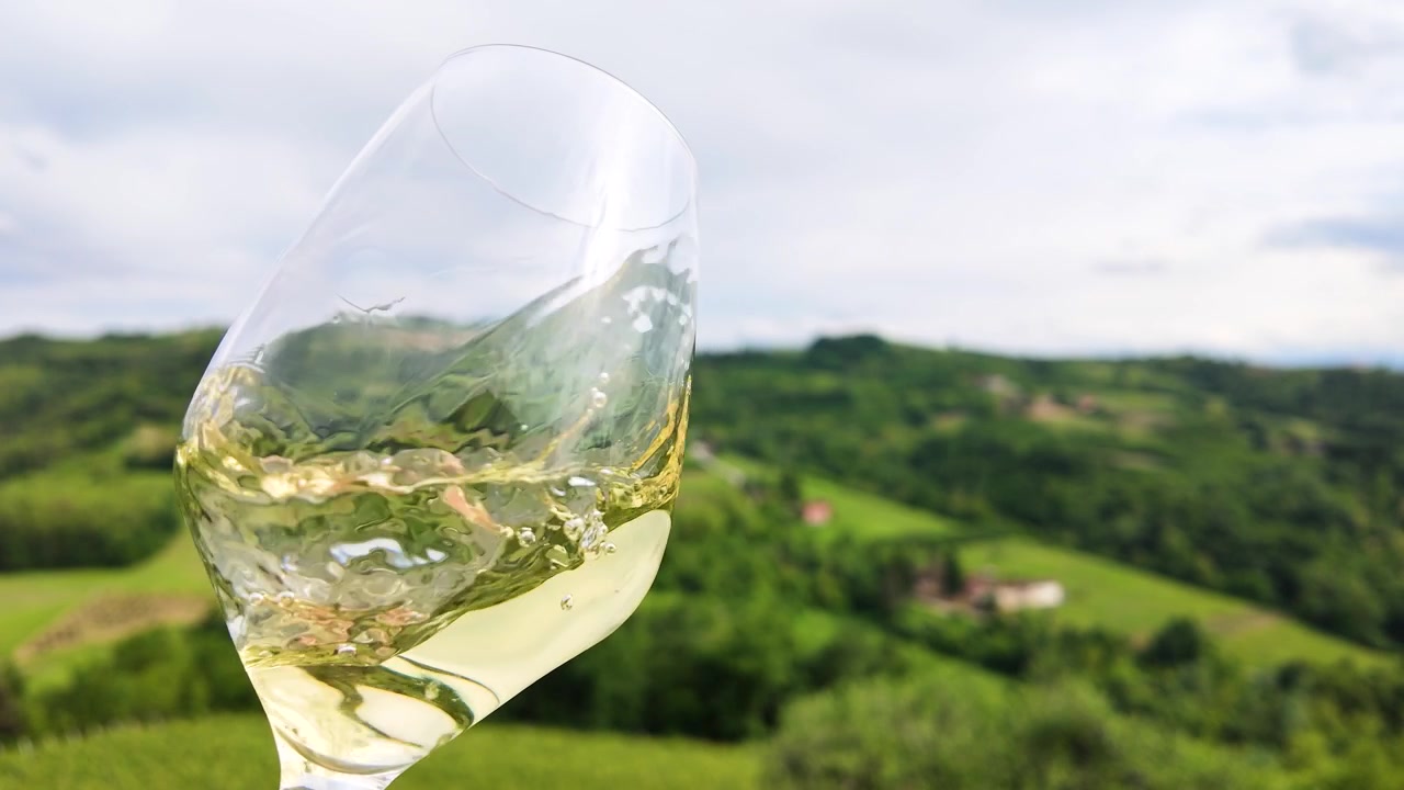 Primo piano di vino bianco che volteggia in un bicchiere sullo sfondo di un paesaggio panoramico di vigneti italiani.