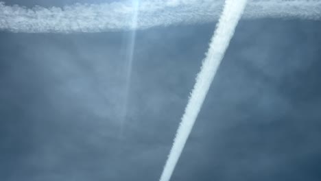vista de cerca tomada desde una cabina de un avión de rayas de escape formando una enorme cruz en un cielo azul con algunas nubes desgastadas y rayos de sol