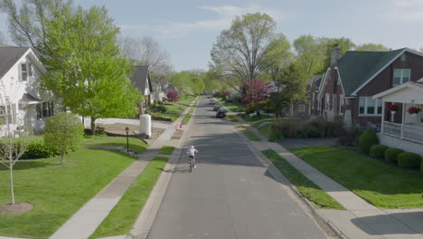 aerial of boy riding his bike down the street and away from camera on a pretty day in the neighborhood