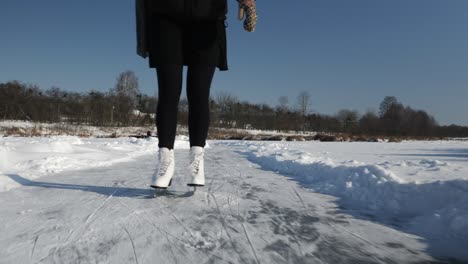 romantic young woman in skirt and white figure skates is skating on frozen river alone. female feet are skating on ice in winter season. outdoor ice-skating