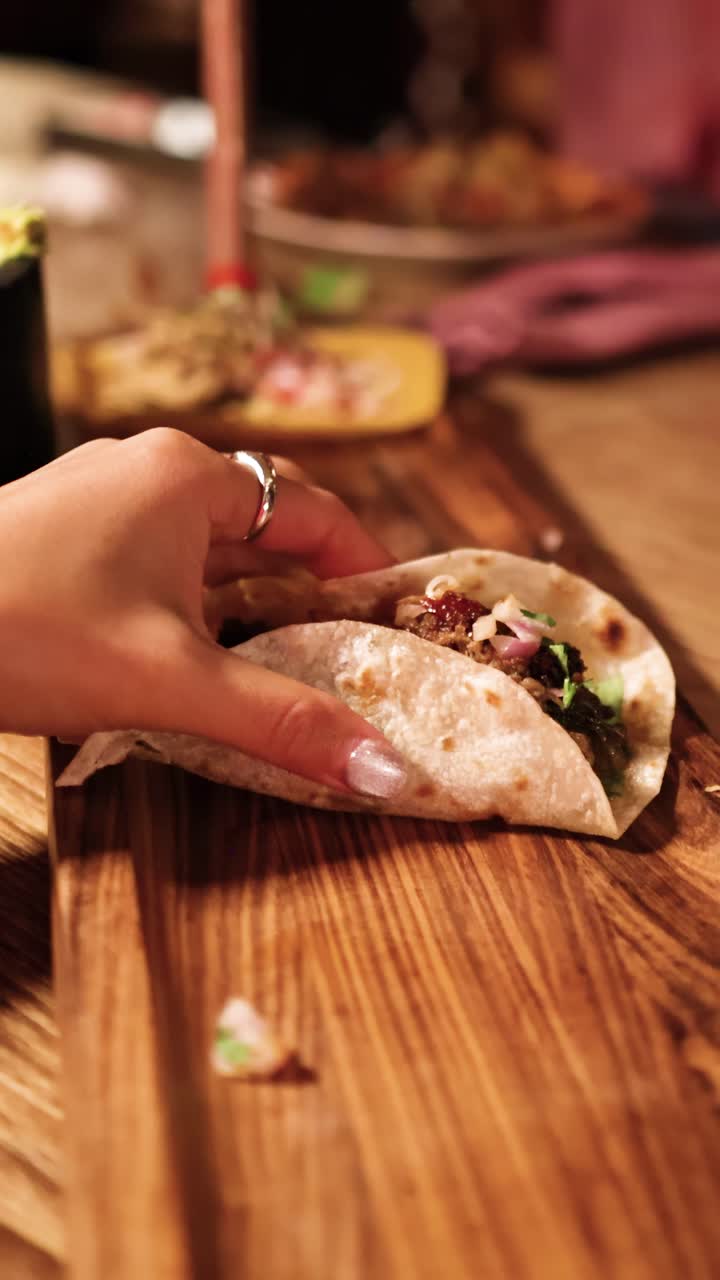 En hånd rækker ud efter en taco på et træbræt i varm belysning, der fanger et afslappet spiseøjeblik