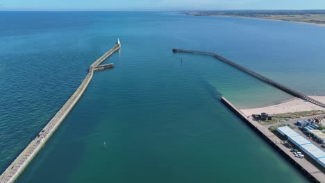 aerial drone clip of calm harbour with jetty wall and picturesque coastline