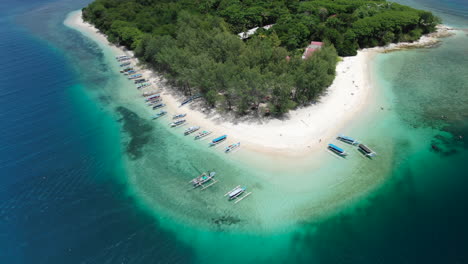 Aerial-drone-tilt-down-shot-as-a-jukung-traditional-boat-arrives-to-a-white-sand-beach-with-tourists