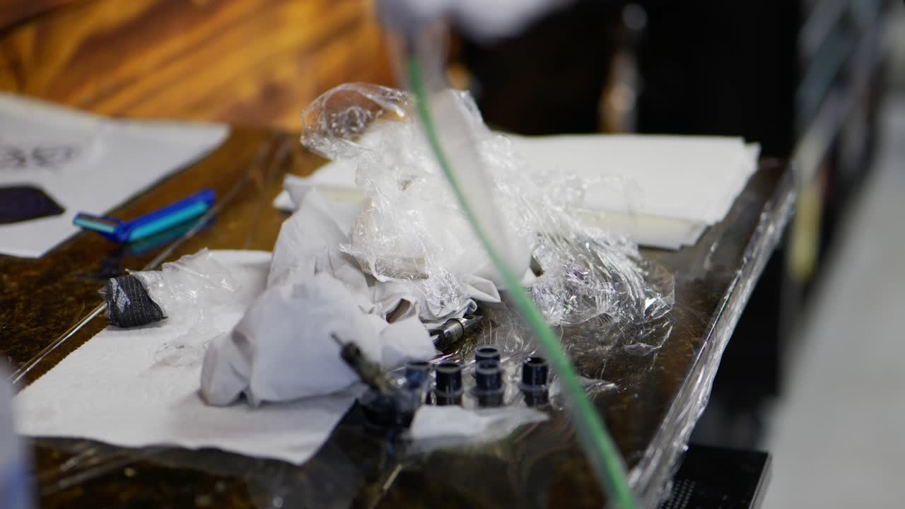 문신 예술가는 작업 후 잉크 컵 바늘 면도기 종이 타월로 지저분한 상점 부스 지역 역을 청소하기 위해 장갑을 벗고 문신을 마쳤습니다.