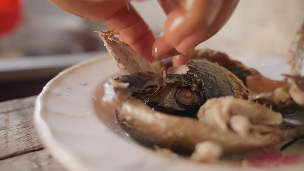 Closeup plate with fish being handled, fingertips pulling tender flesh from small whole fish on vintage ceramic plate, salt flakes and oily sheen, warm kitchen light, tactile homestyle preparation