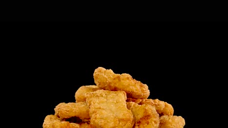 golden brown chicken nuggets spin smoothly against a solid black background, illuminated by even studio lighting. camera movement creates a dynamic, appetizing food presentation