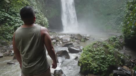 man looking at waterfall in a tropical forest