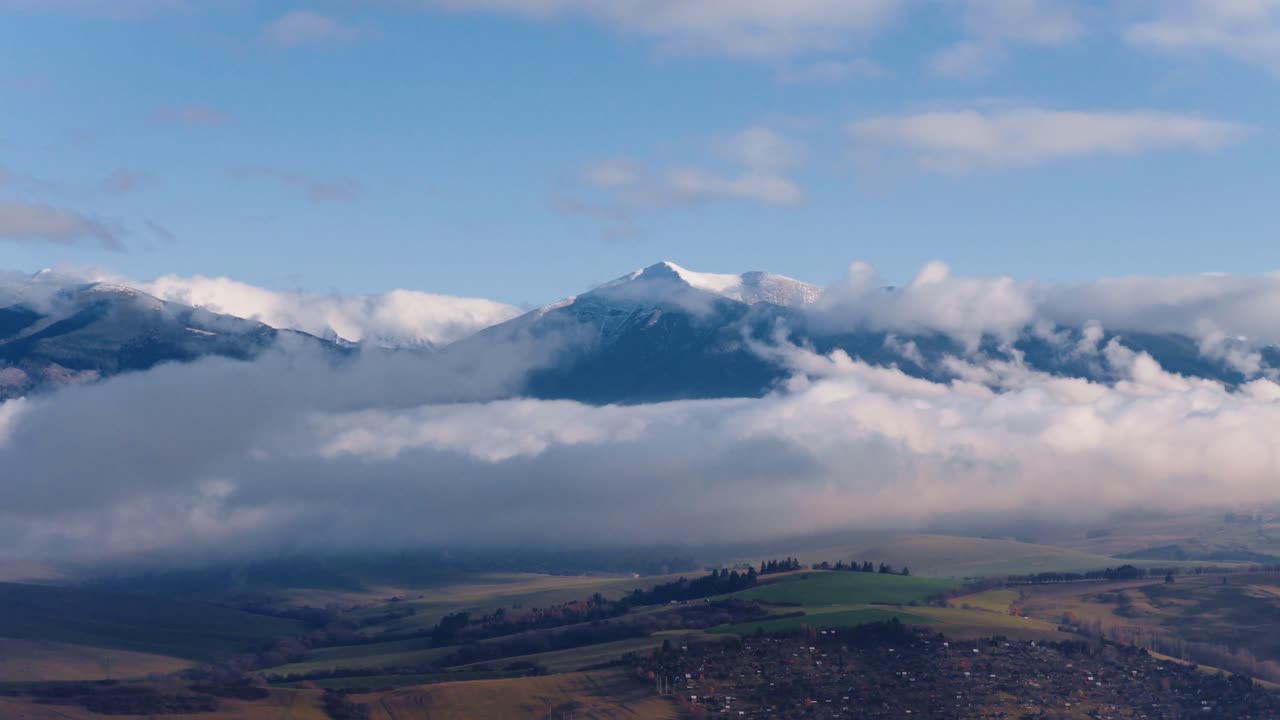 Stunning panorama of the High Tatras in Slovakia, with snowy peaks emerging above drifting clouds and soft light over the rolling landscape below