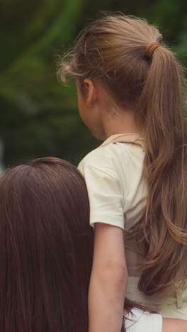 loving mother holds little daughter with spine supporting corset near picturesque waterfall. woman with girl looks at mountain river cascade in forest