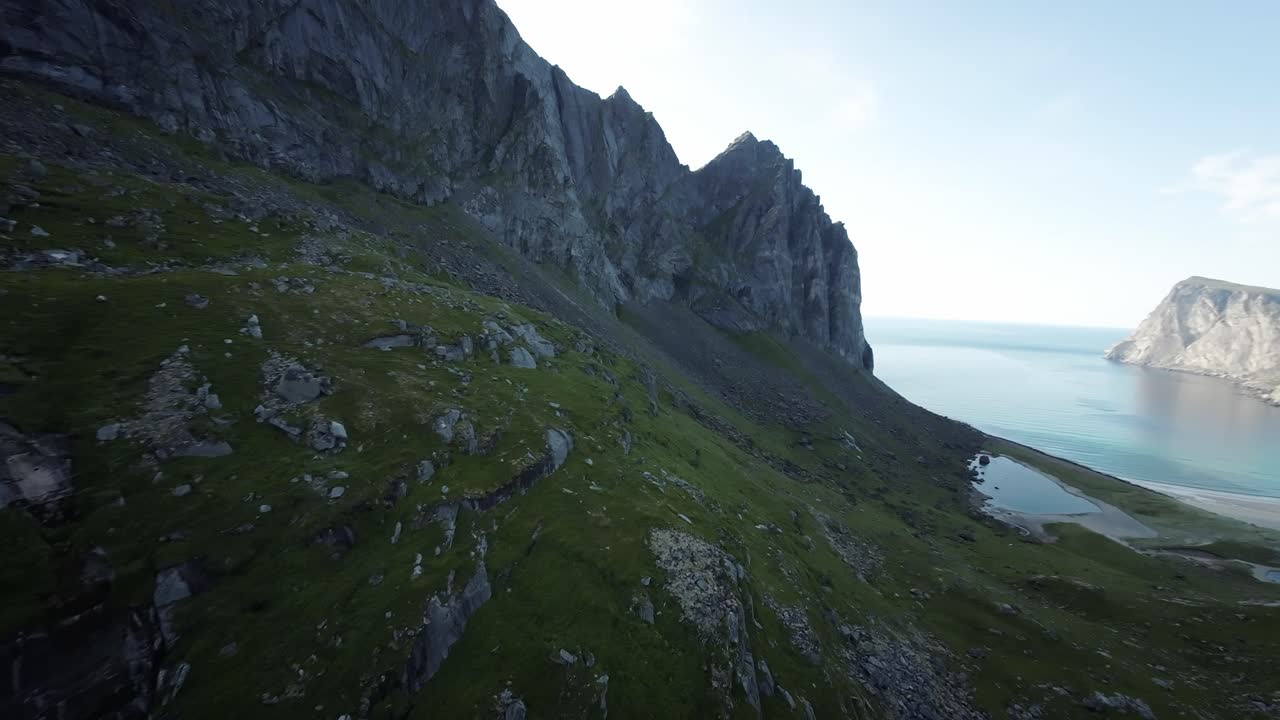 Elokuvamainen, vakaa FPV-dronekuva Lofooteilta, joka paljastaa Kvalvikan rannan vuoristosta.