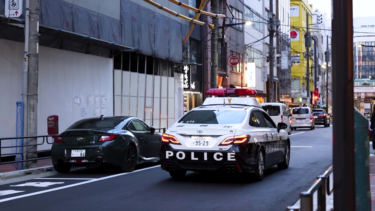 Un véhicule de patrouille noir et blanc roule dans une rue de Tokyo avec des gyrophares rouges clignotants