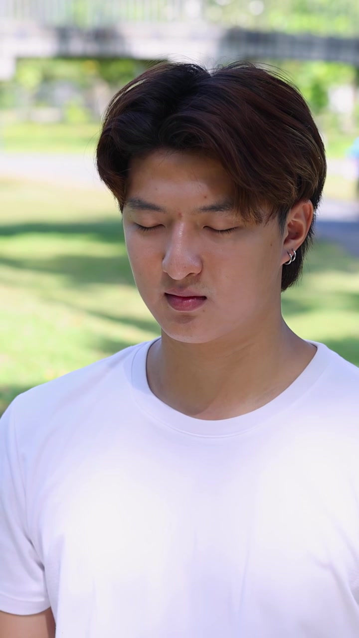 Un giovane uomo asiatico pratica la meditazione mindfulness seduto all'aperto in un parco soleggiato