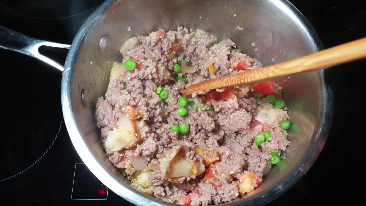 preparación de carne picada - estofado de ternera molida con verduras fritas en mantequilla en una olla de cocina de acero inoxidable en la cocina que se agita con una cuchara de madera